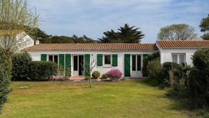 Une maison à deux étages, avec un toit en tuiles, des volets verts et un jardin bien entretenu.