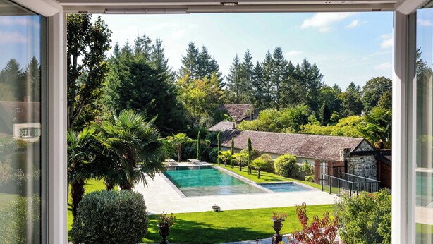 Une piscine entourée d’une végétation luxuriante et d’un bâtiment en pierre.