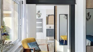 Un salon moderne avec un fauteuil jaune, une table basse en verre et une vue sur la cuisine et l’espace repas.