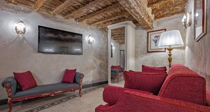 Una habitación con techo de madera, televisor de pantalla plana, sofá, sillón rojo y una lámpara.