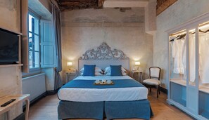 Una camera da letto con un letto grande, due comodini con lampade, una poltrona, una TV e un armadio.