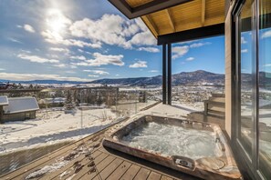 Ein Whirlpool auf einer Holzterrasse mit Blick auf eine verschneite Landschaft und Berge.