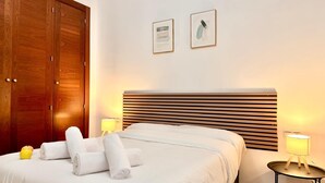 Ein ordentlich bezogenes Bett mit weißen Laken, zwei Nachttischlampen und einem hölzernen Kopfteil.