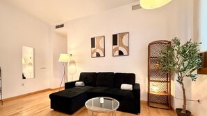 Ein modernes Wohnzimmer mit einem Ecksofa, einem Glastisch und einer Topfpflanze.