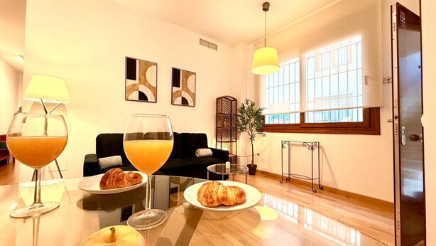 Ein modernes Wohnzimmer mit Essbereich, ausgestattet mit einer Couch, einem Couchtisch mit Frühstücksgebäck und einem großen Fenster, das natürliches Licht hereinlässt.