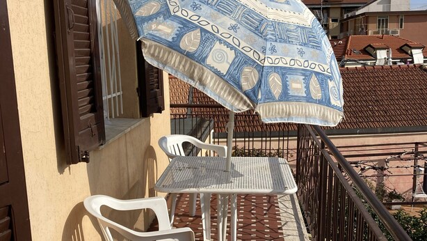 Un balcone con un ombrellone decorato, un tavolo e due sedie.