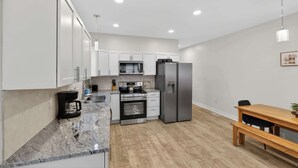 Una cocina moderna con armarios blancos, electrodomésticos de acero inoxidable, encimera de mármol y una mesa de comedor de madera con bancos.