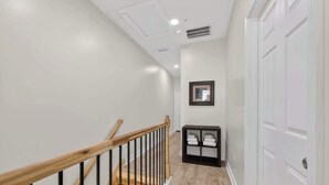 A clean, modern hallway with a wooden staircase, white walls, and a black storage unit.