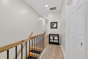 A clean, modern hallway with a wooden staircase, white walls, and a black storage unit. - Cozy Indy Stay - Beville Ave Comfort (Indianapolis)
