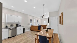 A modern kitchen with white cabinets, a dishwasher, and a dining area with a wooden table and benches.