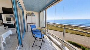 A balcony with a view of the sea, a table with chairs, and a kitchen area. - Le Havre de Paix (Saint-Hilaire-de-Riez)