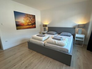 A modern bedroom with a large bed, two bedside tables, and a wall-mounted lamp. - (NEW) Ferienwohnung Brachfeld – Space and relaxation in the Eifel National Park (Hellenthal)
