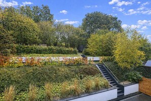 Ein Dachgarten mit einer Treppe, die zu einer Terrasse führt, umgeben von üppigem Grün und Bäumen.