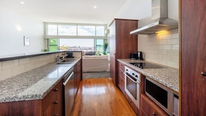 A modern kitchen with granite countertops, stainless steel appliances, and a large window offering a view of the city. - Harborfront Penthouse | Free Parking | Chill Vibes (Auckland)