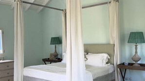 A four-poster bed with white linens, two bedside tables with lamps, and a window with curtains. - Luxury Estate with Private Villas and Family Club House (Bequia)