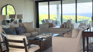 A living room with a large window, a sofa set, a wooden chair, and a coffee table. - Luxury Estate with Private Villas and Family Club House (Bequia)