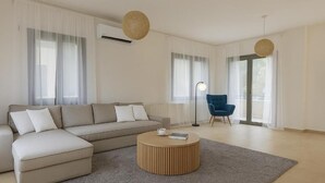 A modern living room with a beige sectional sofa, a round wooden coffee table, and a blue armchair. - Eros Villa Pissouri - Private Pool & Family Friendly (Pissouri)