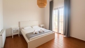 A bedroom with a bed, bedside tables, a radiator, and a window with curtains. - Eros Villa Pissouri - Private Pool & Family Friendly (Pissouri)