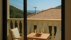 A balcony with a table set for two, a chair, and a view of a building with a tiled roof. - Eros Villa Pissouri - Private Pool & Family Friendly (Pissouri)