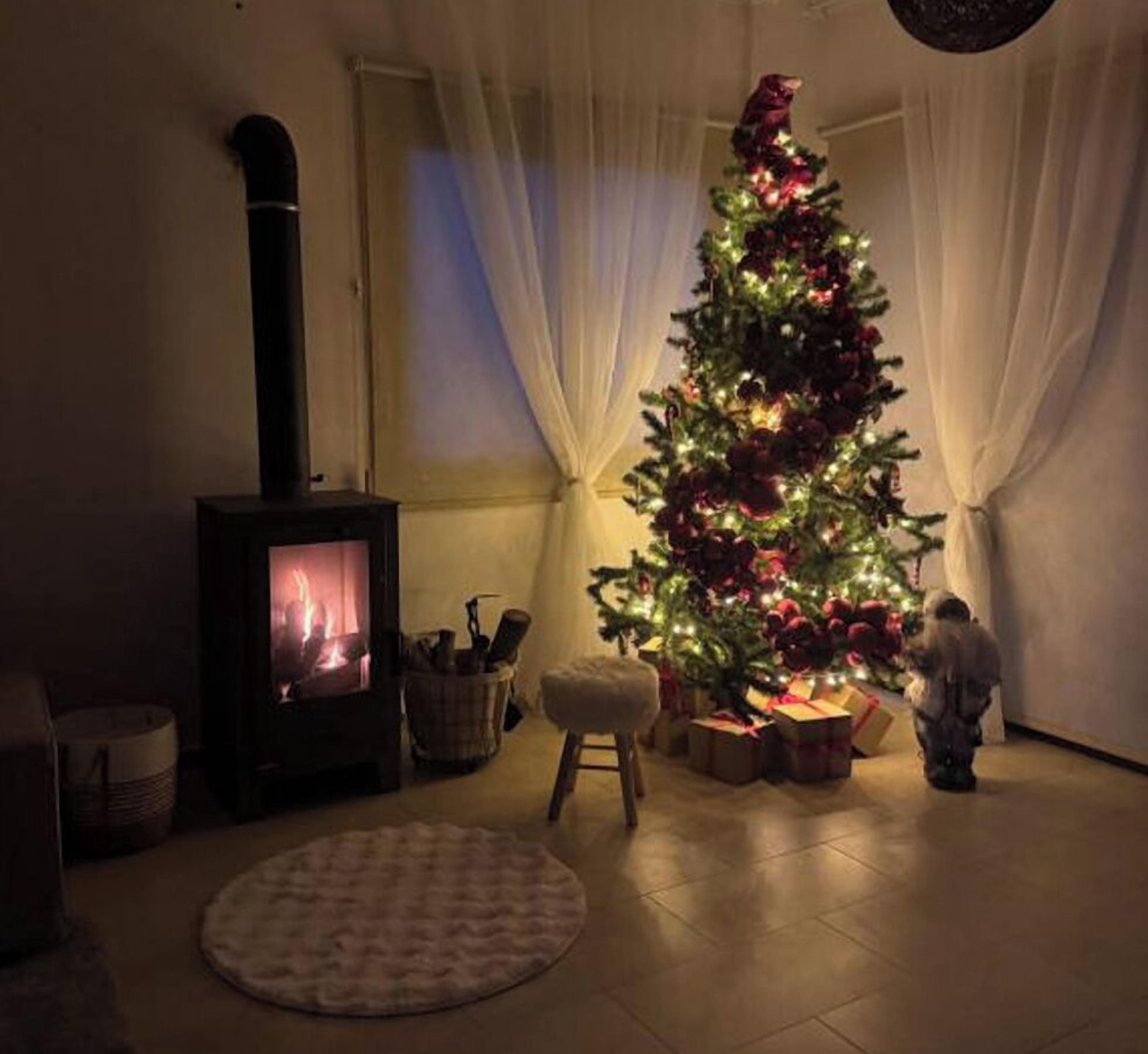 A cozy living room with a fireplace, a decorated Christmas tree, and a child near the tree.