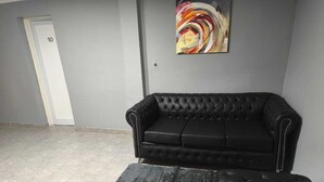 Une pièce avec un canapé en cuir noir, un tapis gris et un tableau abstrait aux couleurs vives accroché au mur.