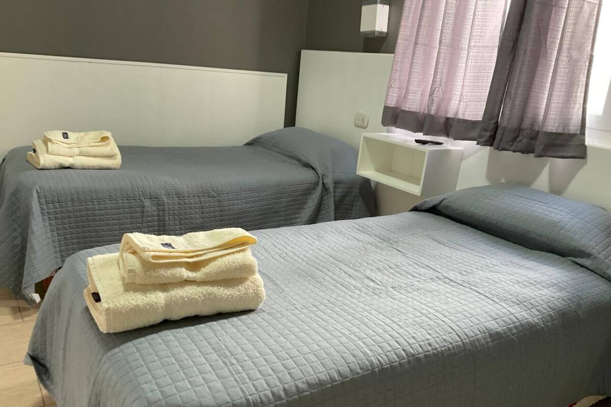 Habitación de hotel con dos camas, cada una con cubrecama gris acolchado y una toalla blanca doblada sobre la cama.