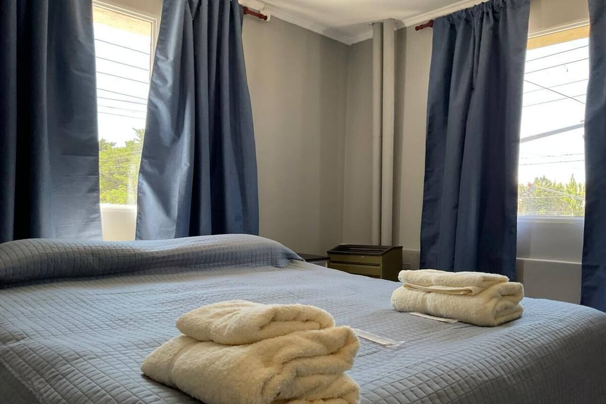 Habitación de hotel con cama, dos toallas, una mesita de noche y una ventana con cortinas.
