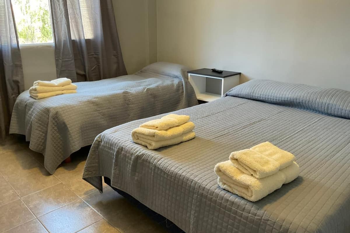 Habitación de hotel con dos camas, cada una con una toalla doblada, una mesita de noche con un control remoto y una ventana con cortinas.