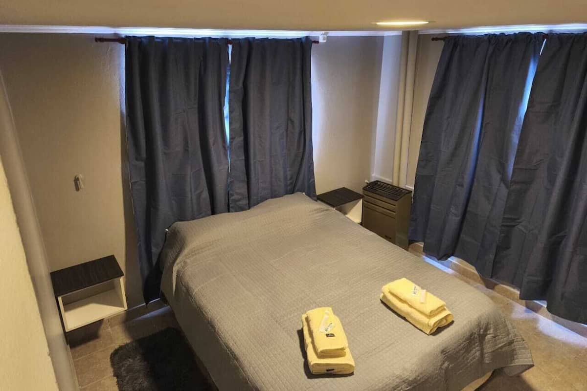 Un dormitorio pequeño y ordenado, con cama, dos mesitas de noche y un armario pequeño.