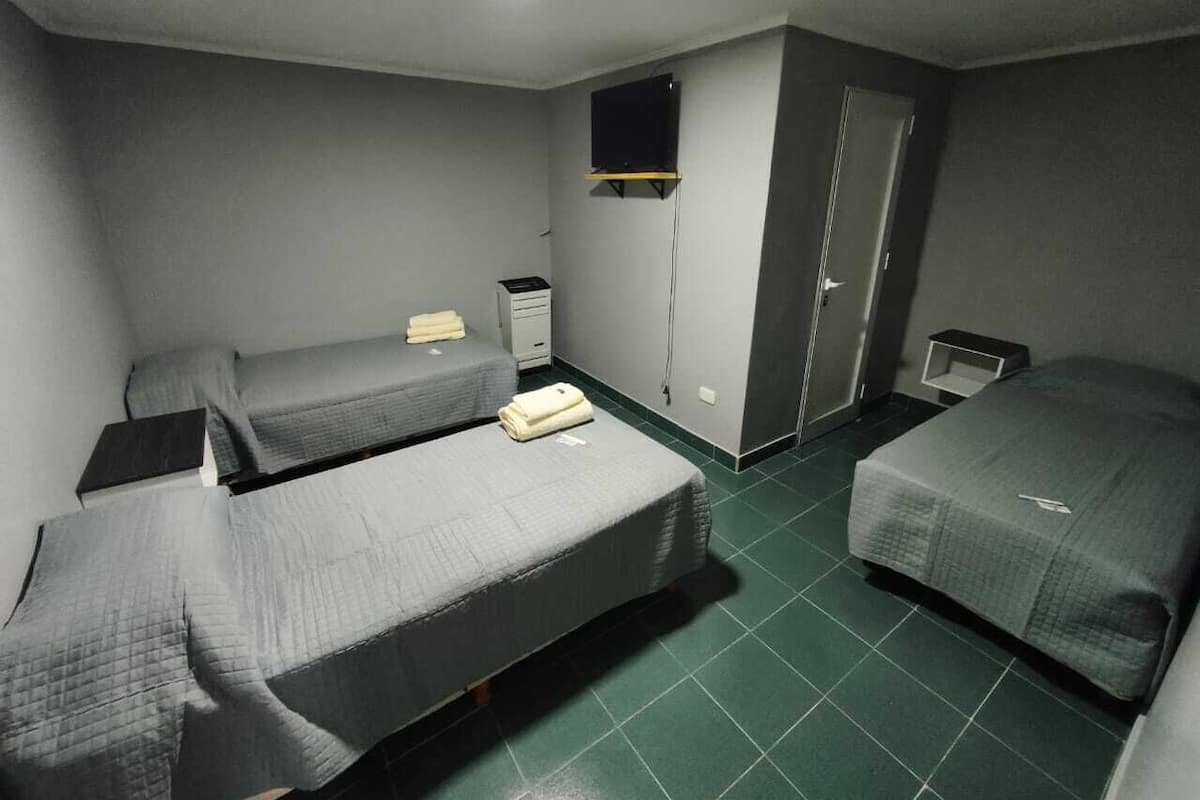Una habitación con tres camas individuales, un televisor montado en la pared, un escritorio y un armario.