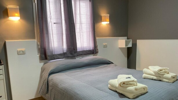 Une chambre à coucher avec un lit, deux lampes fixées au mur, une fenêtre avec des rideaux et deux serviettes pliées posées sur le lit.