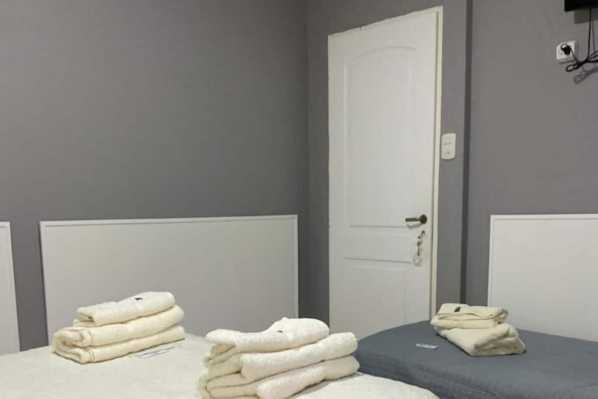 Un dormitorio con dos camas, una con colcha blanca y la otra con colcha azul. Hay toallas dobladas sobre cada cama.