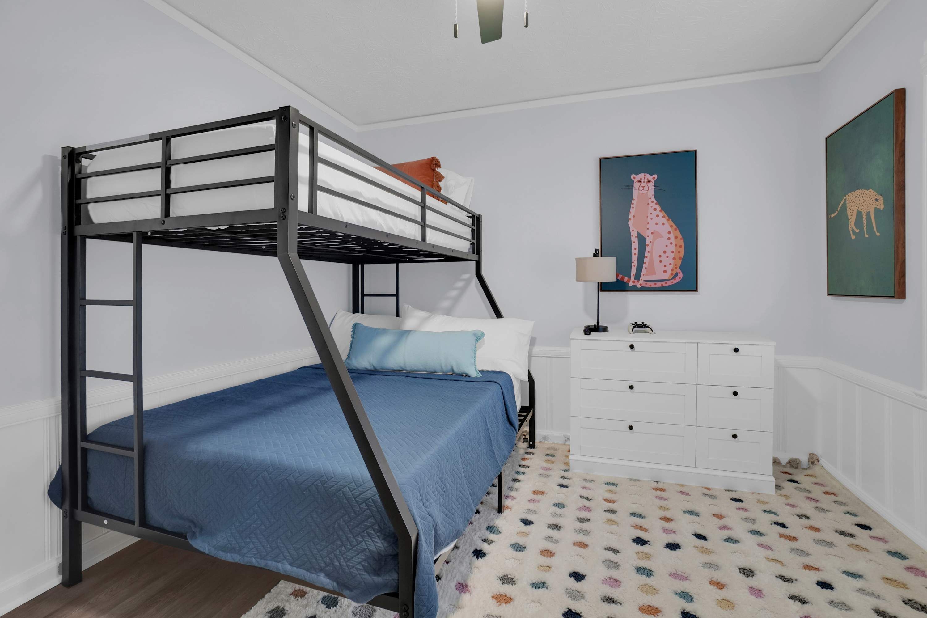 Un lit superposé avec un matelas bleu, des oreillers blancs et une commode blanche à tiroirs.