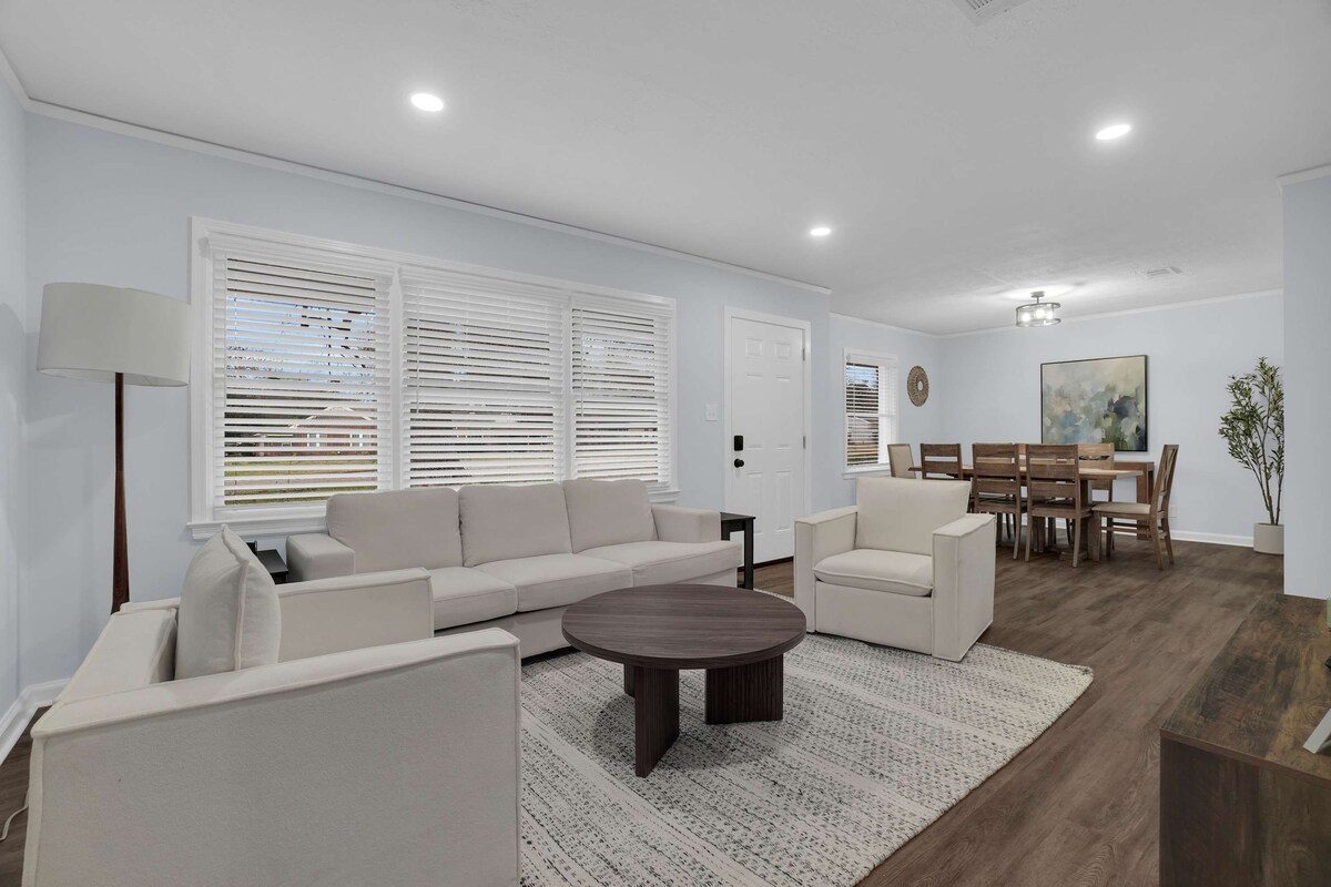 A modern living room with a sofa, armchairs, a coffee table, and a dining area with a table and chairs.
