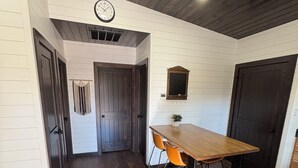 A room with a wooden table and two chairs, a clock on the wall, and a door leading to another room. - Cozy new construction 2-bedroom house in serene Harrison with all amenities. (Harrison)