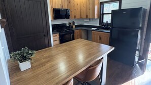 A modern kitchen with wooden cabinets, a black refrigerator, and a wooden dining table with two chairs. - Cozy new construction 2-bedroom house in serene Harrison with all amenities. (Harrison)