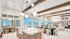 Una cocina amplia con una isla grande, iluminación colgante moderna y ventanas grandes con vistas al océano.