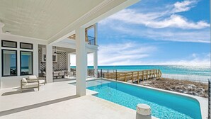 Un área de piscina moderna con vista despejada al océano, una terraza de madera y un espacio de descanso con asientos.