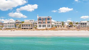 Una propiedad frente a la playa con varias casas, incluyendo una casa de dos pisos destacada, con amplias ventanas y un balcón.