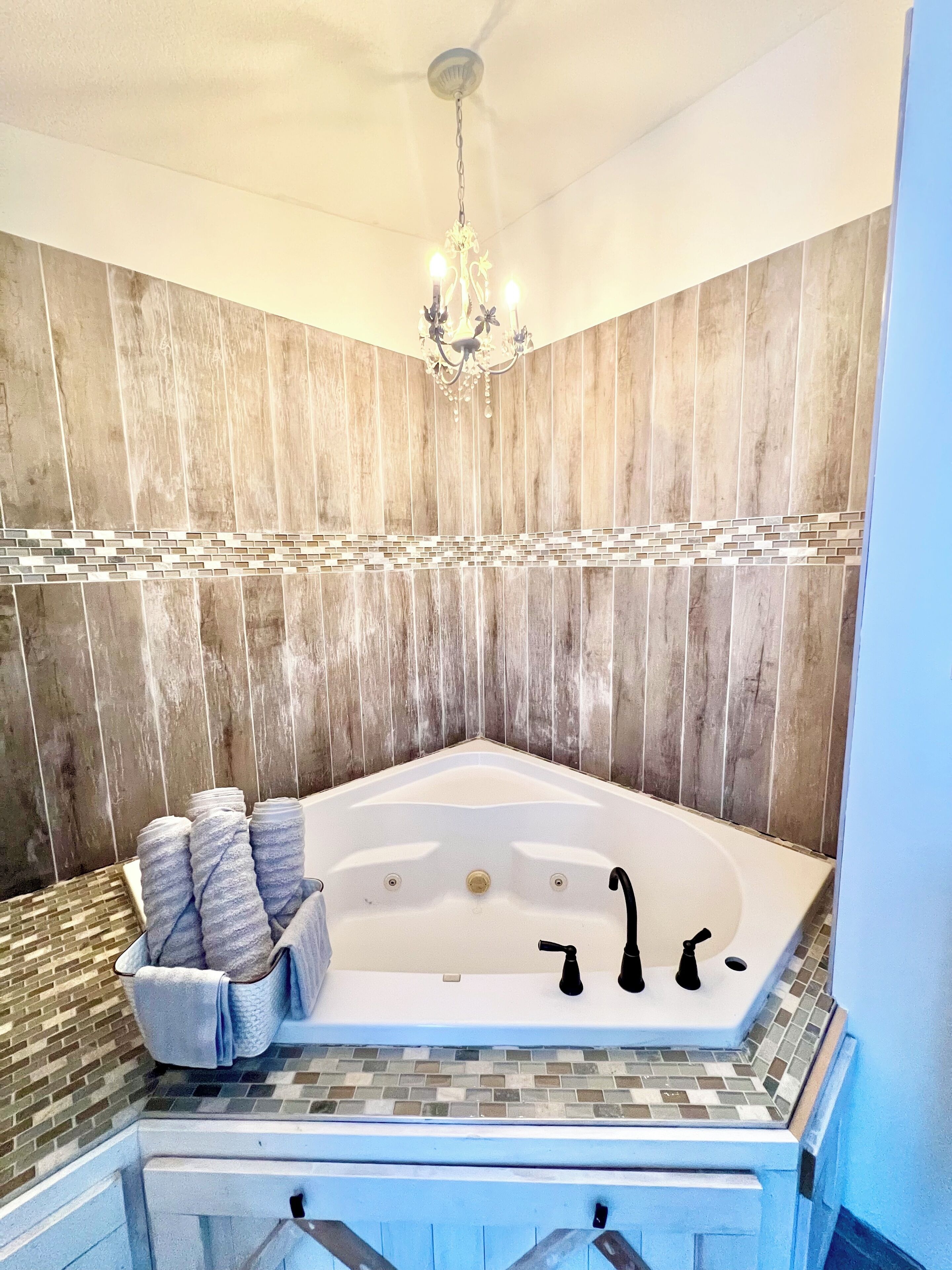A modern bathroom with a freestanding bathtub, a chandelier, and a tiled backsplash.