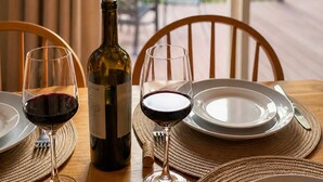 A dining table with a bottle of wine, two wine glasses, and plates, set against a backdrop of a deck and greenery. - Parkway Paradise Cozy Retreat Blue Ridge Parkway Family & Pet Friendly  (Laurel Springs)
