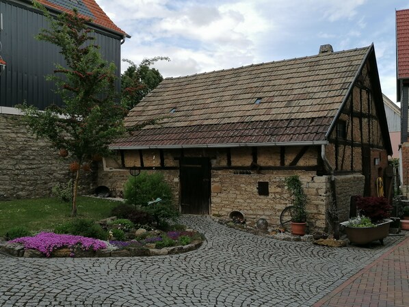 Ein traditionelles Fachwerkhäuschen mit einem Kopfsteinpflasterhof, Steinmauern und einem kleinen Garten mit Blumen.