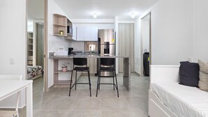 A compact kitchen with a central island, two bar stools, and a dining table. - Luxury & Calm in Serena del Mar: Your New Retreat at Capriella (cartagena)