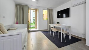 A modern, well-lit room with a ceiling fan, a flat-screen TV mounted on the wall, a dining table with chairs, and a sliding glass door leading to a balcony. - Luxury & Calm in Serena del Mar: Your New Retreat at Capriella (cartagena)