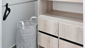A closet with multiple shelves and hanging space, a striped laundry basket, and a metal rod for hanging items. - Luxury & Calm in Serena del Mar: Your New Retreat at Capriella (cartagena)