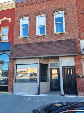A two-story brick building with a storefront, large windows, and a black door.