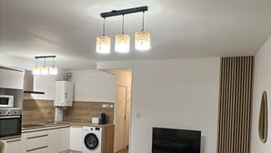 Um apartamento moderno com sala de estar, cozinha e espaço de jantar. Possui um sofá, uma mesa de centro, uma TV e uma máquina de lavar.