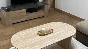 Uma sala de estar moderna com uma televisão de tela plana, um móvel para aparelhos eletrônicos de madeira, uma mesa de centro redonda com velas e um espelho grande na parede.