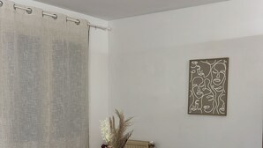 Uma área de refeições com uma mesa redonda, quatro cadeiras, um vaso com plantas secas e uma obra de arte na parede.