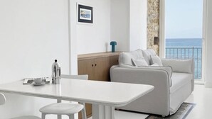 Uma sala de estar moderna e minimalista, com um sofá branco e uma área de jantar com mesa e cadeiras brancas.